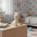Pepper & White Alpine Alpaca shaped cream wax candle standing on a wooden nursery table with plush toys in background