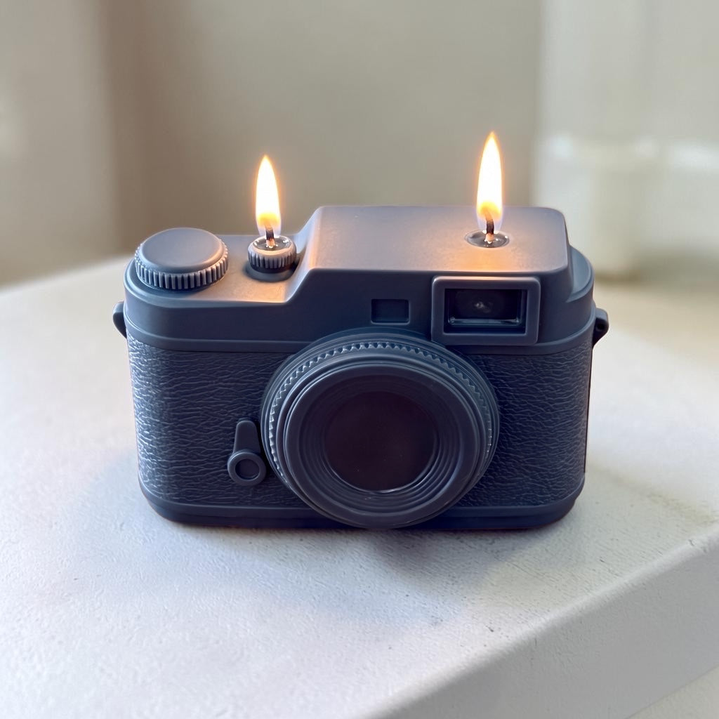 Pepper & White charcoal grey vintage camera shaped wax candle with two lit wicks on a neutral surface