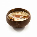 Pepper & White Coconut Grove candle in a natural coconut shell bowl with dried flower petals and a wooden wick