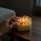 Pepper & White decorative glass jar candle with yellow wax roses and dried baby's breath, lit on a wooden table.
