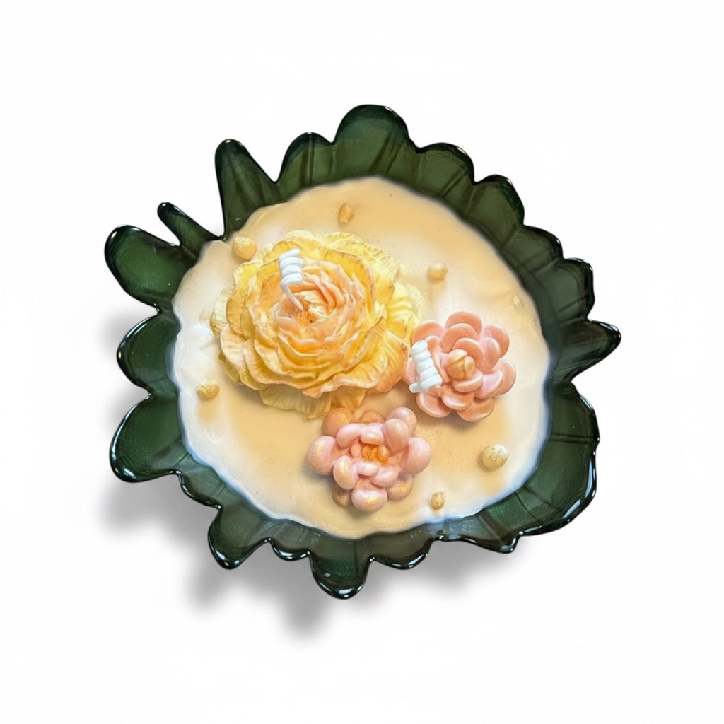 Pepper & White decorative soy wax candle in a forest green scalloped glass bowl with yellow and pink floral sculptures.