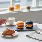 Pepper & White Happy Meal Freesia candles shaped like smiling cheeseburgers on a slate board with a croissant and tea.