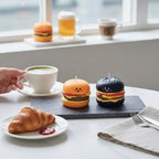 Pepper & White Happy Meal Freesia candles shaped like smiling cheeseburgers on a slate board with a croissant and tea.