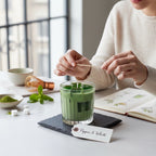 Pepper & White matcha latte scented candle in a glass tumbler on a slate coaster with matcha powder and a whisk