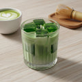 Pepper & White Matcha Latte candle in a ribbed glass tumbler with green wax ice cubes on a wooden table.
