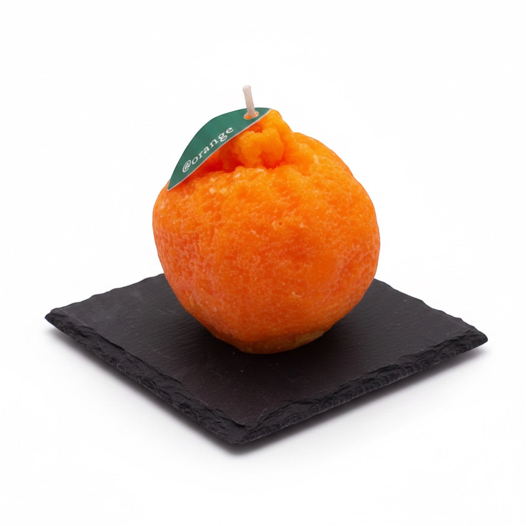 Pepper & White orange-shaped decorative wax candle with a green leaf tag on a square black slate coaster