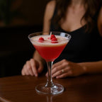 Pepper & White Scarlet Sip strawberry martini candle in a glass with wax raspberry toppings on a wooden table.