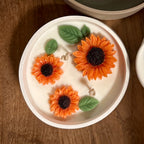 Pepper & White sunflower shaped soy wax candle with three wicks in a white ceramic bowl on a wooden surface.