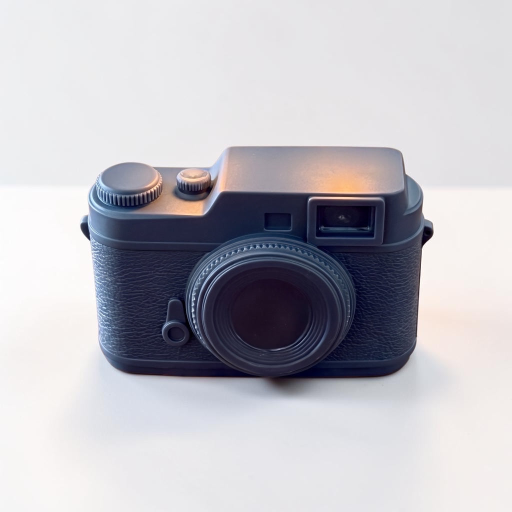 Pepper & White charcoal grey vintage rangefinder camera shaped wax candle with textured detailing on a white surface